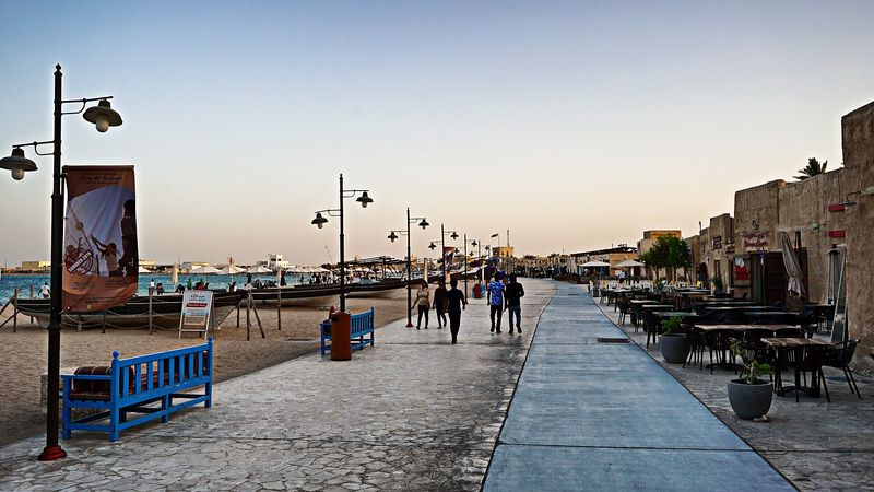 Seafront promenade of Al Wakrah Souq at dusk, with wooden boats drawn up on the beach