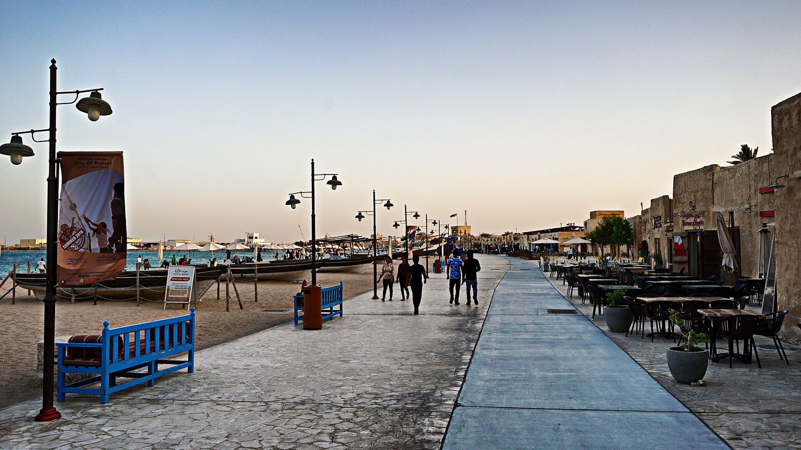 Seafront promenade of Al Wakrah Souq at dusk, with wooden boats drawn up on the beach