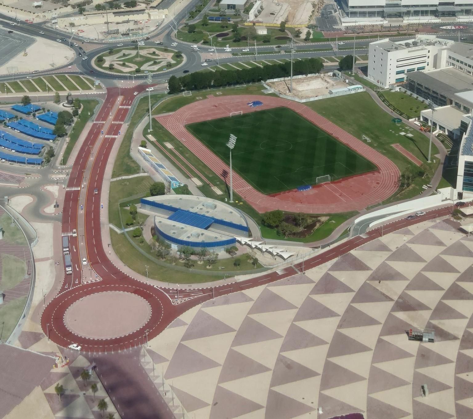 Aspire Zone from above: a training pitch and running track beside a patterned pedestrian plaza