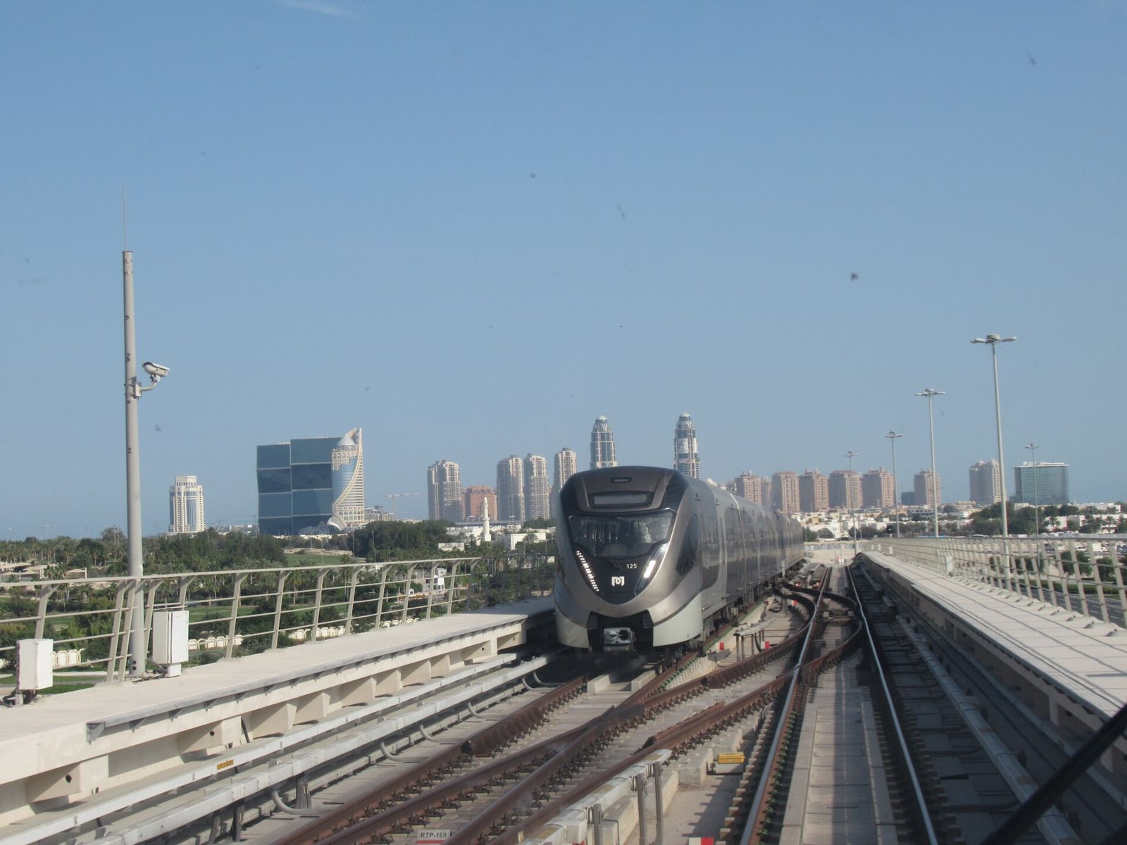 A Doha Metro train approaching on an elevated stretch of the Red Line, with high-rise towers on the horizon