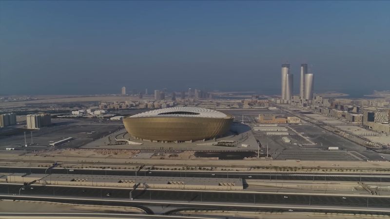 Aerial view of the golden bowl of Lusail Stadium, with Lusail's high-rise towers in the background